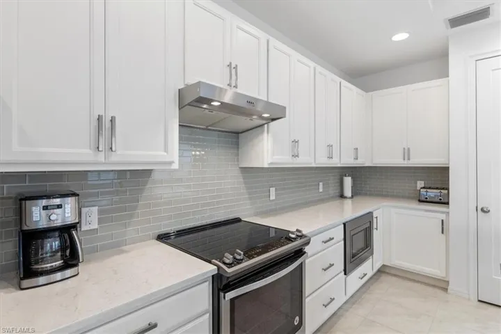 Kitchen featuring range with electric stovetop, stainless steel microwave, decorative backsplash, and light tile patterned floors