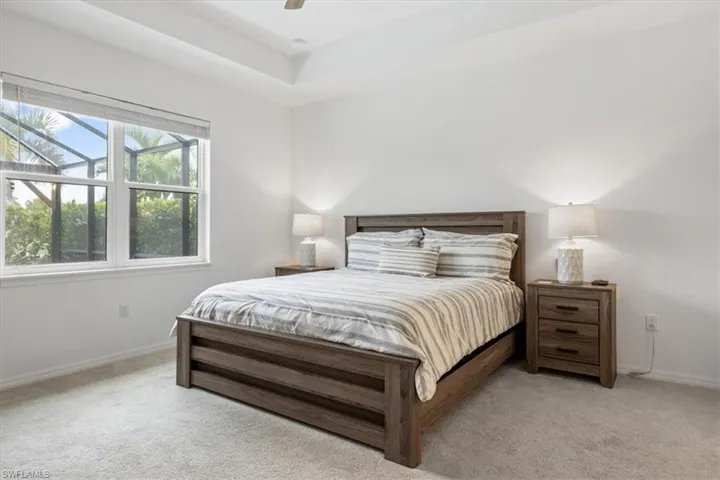 Bedroom featuring light carpet, ceiling fan, and a tray ceiling