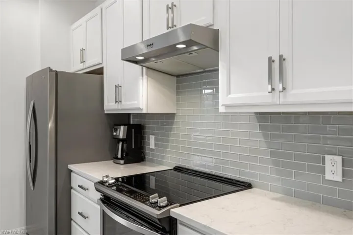 Kitchen featuring decorative backsplash, stainless steel electric range oven, light stone counters, and white cabinets