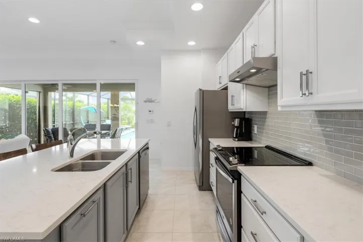Kitchen featuring wall chimney exhaust hood, sink, appliances with stainless steel finishes, light tile patterned floors, and backsplash