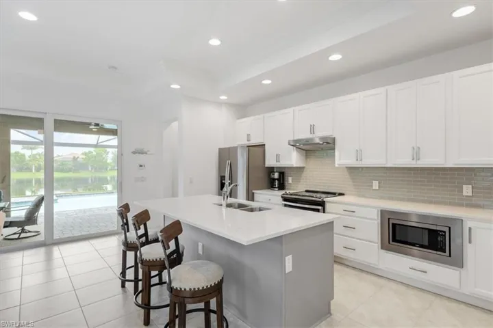 Kitchen with light tile patterned floors, white cabinets, stainless steel appliances, decorative backsplash, and a center island with sink