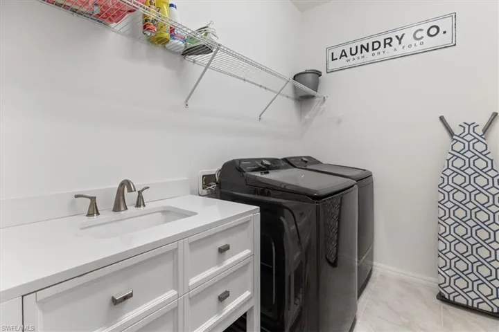 Laundry area with light tile patterned flooring, independent washer and dryer, sink, and cabinets