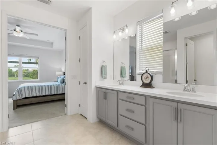 Bathroom featuring tile patterned flooring, a tray ceiling, ceiling fan, and dual bowl vanity