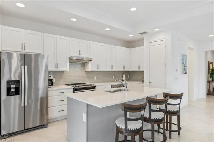 Kitchen with stainless steel appliances, white cabinets, sink, decorative backsplash, and light tile patterned flooring