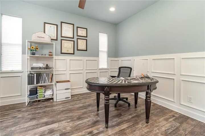 Den/office area with wainscoting, ceiling fan and dark wood-type flooring