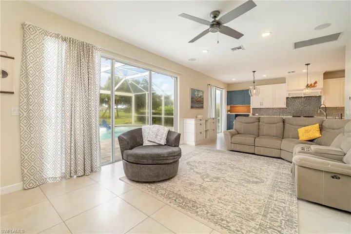 Tiled living room with ceiling fan and two slider doors to pool/lanai area