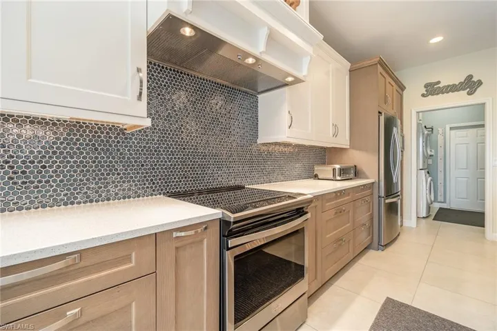 Kitchen featuring light brown cabinets, beautiful backsplash, exhaust hood, and stainless steel appliances