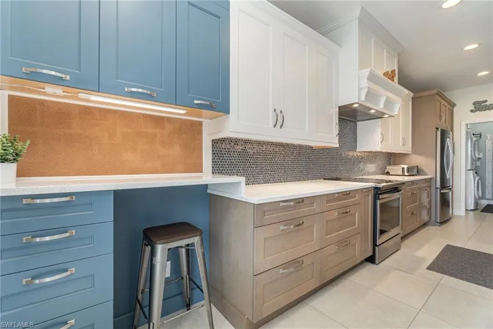 Kitchen featuring white cabinetry, tasteful backsplash, light tile patterned floors, stainless steel appliances, and desk/work area