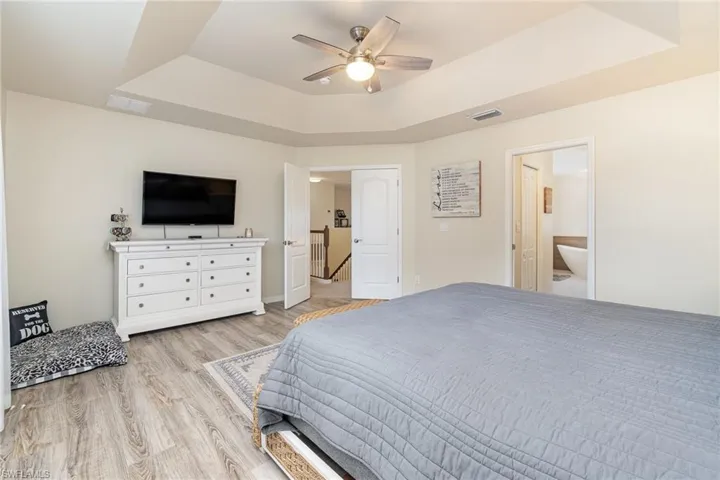 Bedroom featuring a tray ceiling, ceiling fan, ensuite bathroom, and light hardwood / wood-style flooring