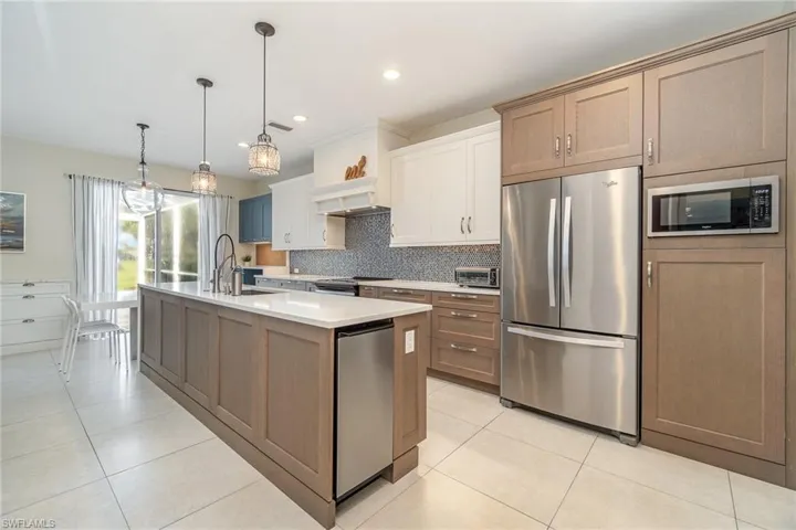 Kitchen with a kitchen island with sink, backsplash, stainless steel appliances, and decorative light fixtures