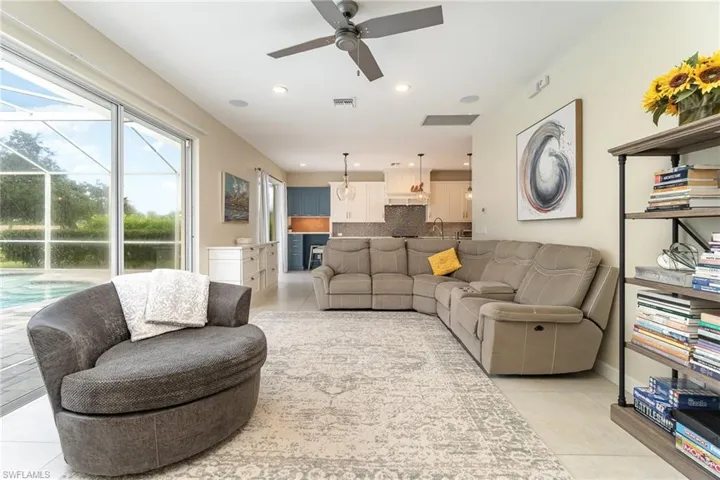 Living room with light tile patterned floors, ceiling fan, and slider doors to lanai/pool area