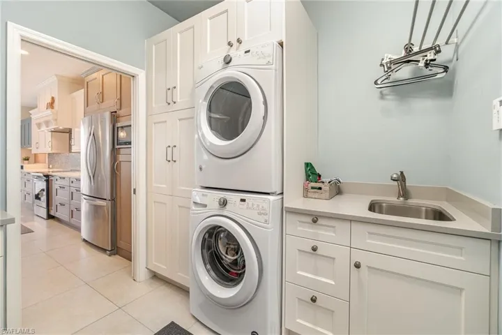 Stacked washer and dryer, light tile patterned flooring, sink, and cabinets