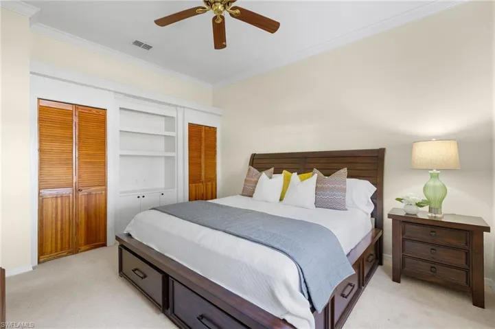 Bedroom featuring ornamental molding, multiple closets, light carpet, and ceiling fan