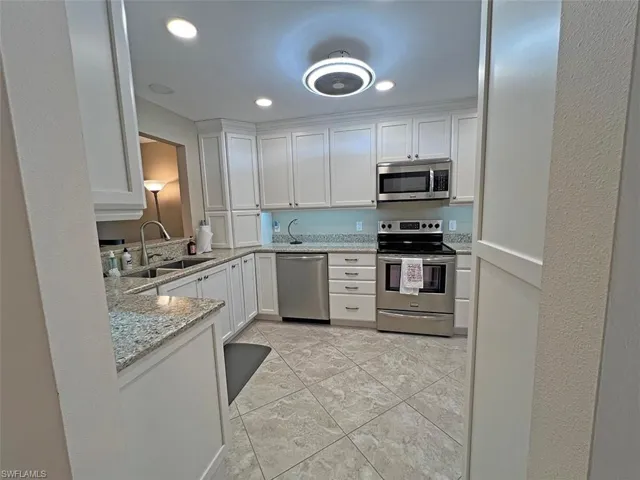 Beautifully updated eat-in kitchen with stainless steel appliances, white cabinets, light stone counters, and recessed lighting
