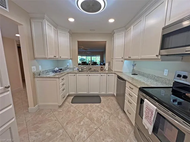 Beautifully updated eat-in kitchen with stainless steel appliances, white cabinets, light stone counters, and recessed lighting