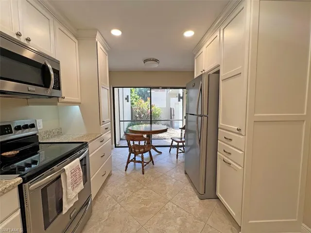Beautifully updated eat-in kitchen with stainless steel appliances, white cabinets, light stone counters, and recessed lighting