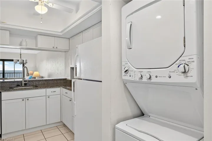 Washroom featuring light tile patterned floors, stacked washer / drying machine, a ceiling fan, and a chandelier