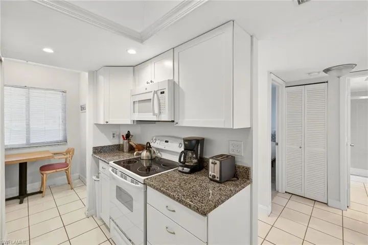 Kitchen with white appliances, light tile patterned flooring, white cabinetry, ornamental molding, and recessed lighting