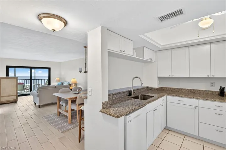 Kitchen featuring dark stone countertops, white cabinetry, white dishwasher, and open floor plan