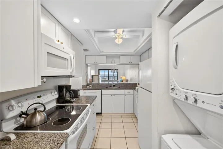 Kitchen featuring white appliances, white cabinetry, light tile patterned floors, a raised ceiling, and ceiling fan