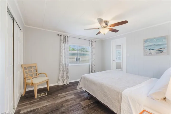 Bedroom with crown molding, dark wood finished floors, wooden walls, ceiling fan, and a closet