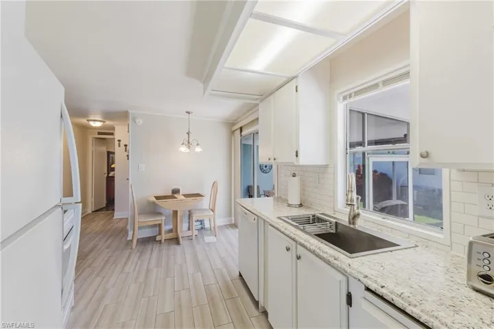 Kitchen featuring white appliances, a chandelier, hanging light fixtures, white cabinetry, and decorative backsplash
