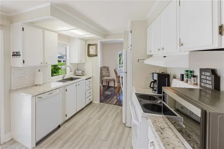 Kitchen with light countertops, white appliances, wood tiled floors, white cabinets, and decorative backsplash