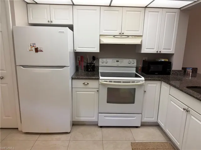 Kitchen featuring white appliances, dark stone countertops, white cabinets, and light tile patterned floors