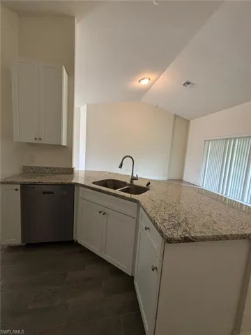 Kitchen with white cabinetry, a peninsula, dishwasher, light stone counters, and lofted ceiling