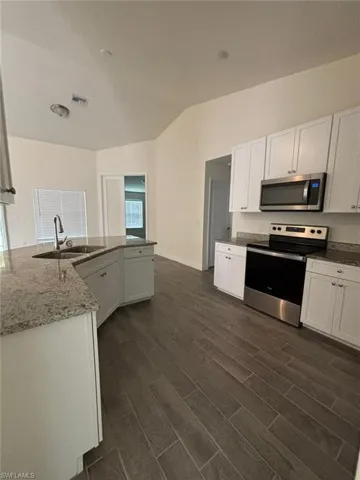Kitchen featuring appliances with stainless steel finishes, dark stone counters, white cabinetry, dark wood-style flooring, and lofted ceiling