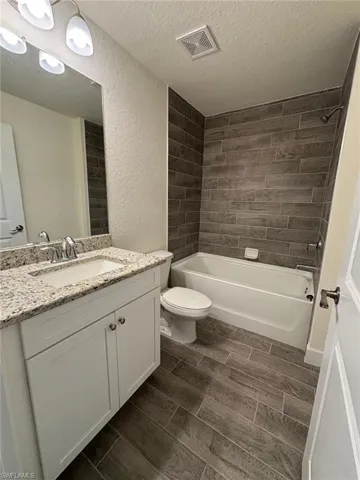 Bathroom featuring shower / bath combination, wood finish floors, vanity, a textured ceiling, and a textured wall