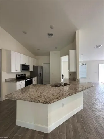 Kitchen with wood finish floors, white cabinetry, light stone countertops, appliances with stainless steel finishes, and a peninsula