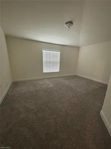 Unfurnished room featuring dark carpet and lofted ceiling