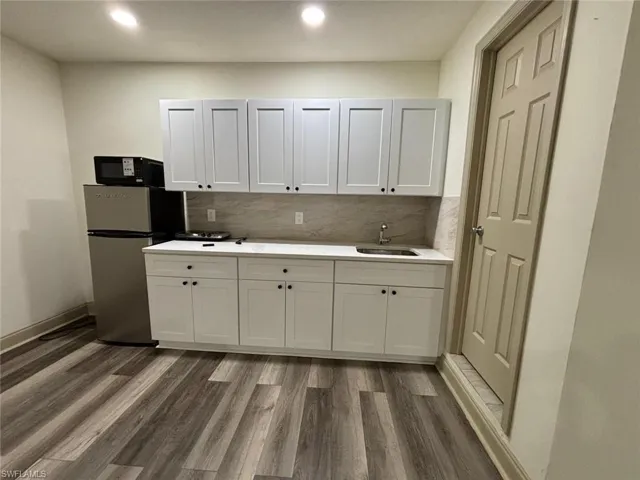 Kitchen with dark wood-style flooring, freestanding refrigerator, white cabinets, decorative backsplash, and recessed lighting