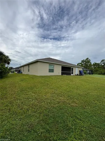 Rear view of property featuring a lawn, stucco siding, and a sunroom