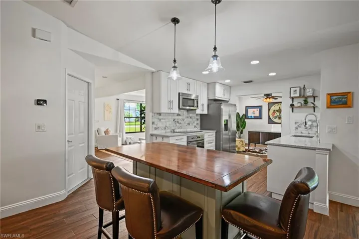 Kitchen featuring white cabinetry, dark stone counters, decorative backsplash, a breakfast bar area, and dark wood finished floors