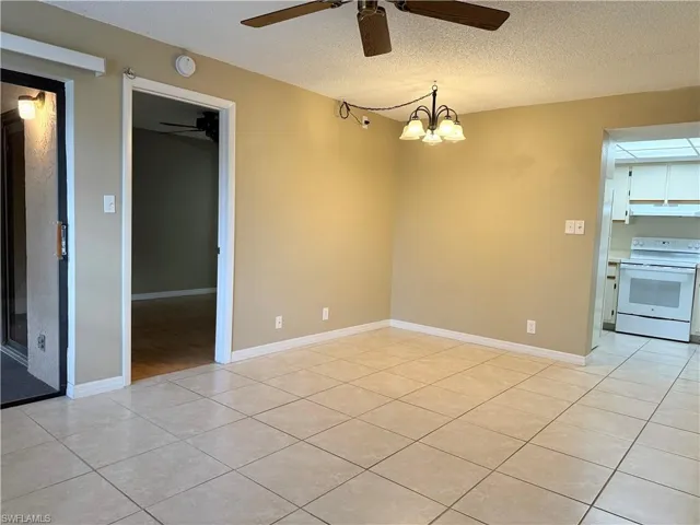 Tiled empty room featuring a textured ceiling and a chandelier