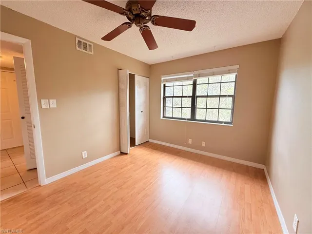 Unfurnished bedroom with a textured ceiling, light hardwood / wood-style flooring, ceiling fan, and multiple closets