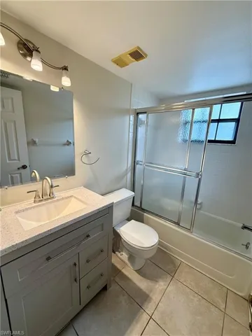 Full bathroom with shower / bath combination with glass door, toilet, tile patterned floors, and vanity