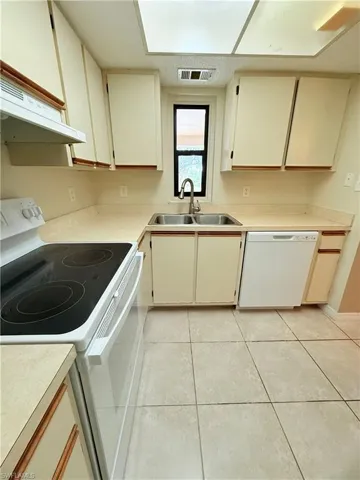 Kitchen with white appliances, exhaust hood, sink, light tile patterned floors, and cream cabinetry