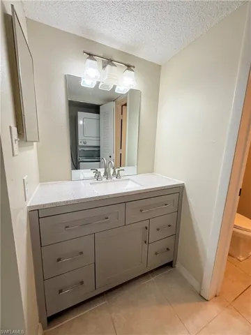 Bathroom with toilet, stacked washer and dryer, a textured ceiling, and tile patterned flooring