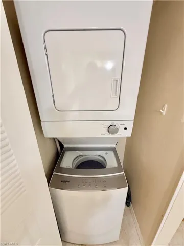 Washroom featuring light tile patterned flooring and stacked washing maching and dryer