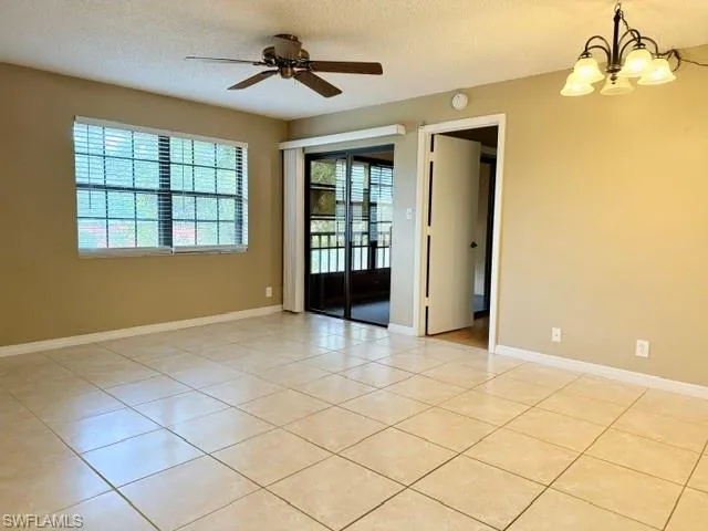 Tiled spare room with a textured ceiling and ceiling fan with notable chandelier
