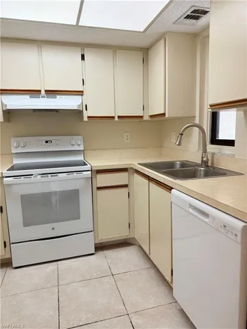 Kitchen with cream cabinetry, white appliances, sink, and light tile patterned floors