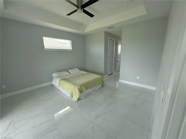 Unfurnished bedroom with tile patterned floors, ceiling fan, and a raised ceiling
