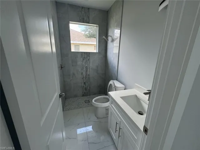 Bathroom featuring vanity, tile patterned floors, tiled shower, and toilet