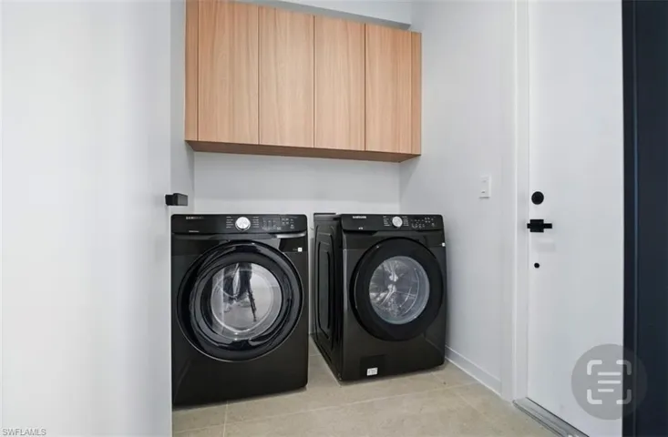 Laundry area featuring washer and clothes dryer, cabinet space, and light tile patterned floors