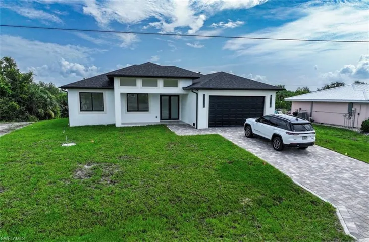 Prairie-style home featuring a front yard, stucco siding, decorative driveway, and an attached garage