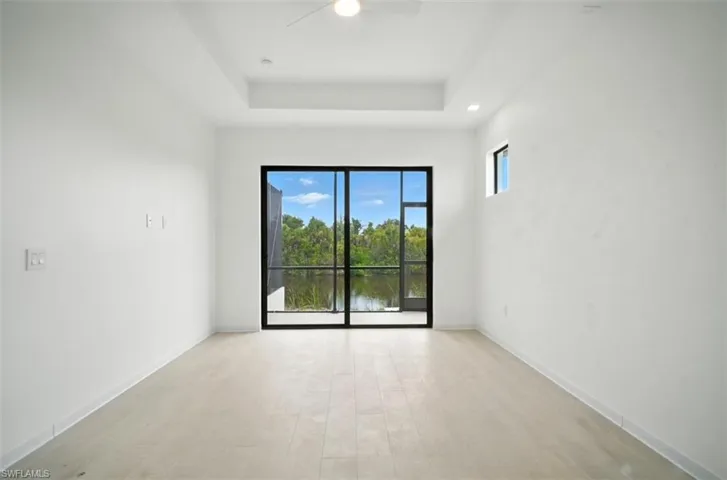 Unfurnished room featuring light wood-style flooring, ceiling fan, a water view, and a raised ceiling