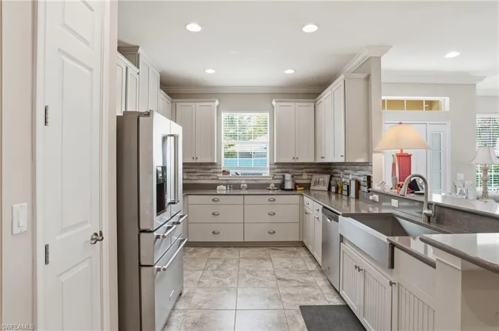 Spacious kitchen featuring white cabinetry, stainless steel appliances, a farmhouse sink, stone countertops, and a tile backsplash